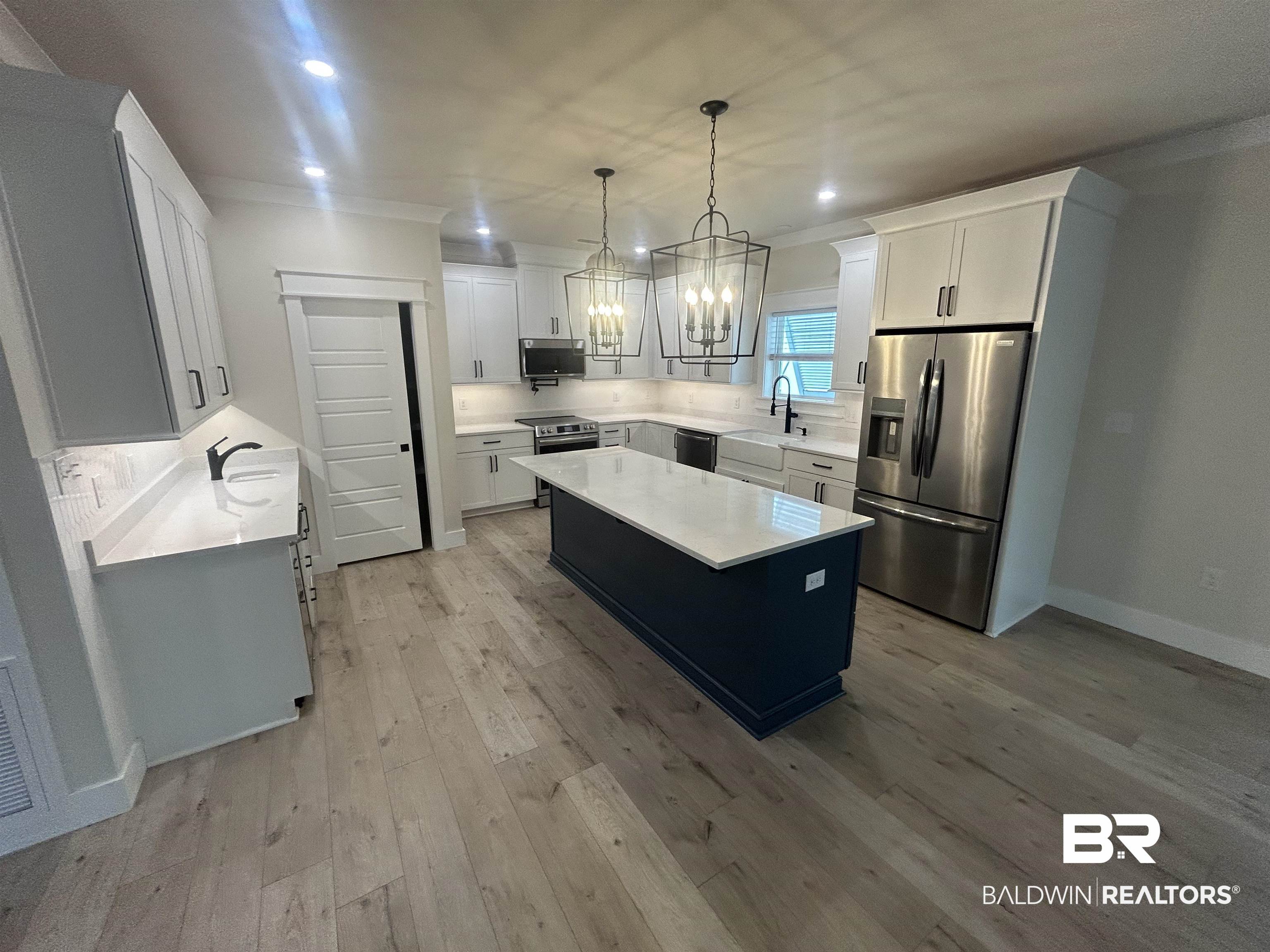 5122 Pine Road Orange Beach, AL 36561 - Photo 5 of 24 Two tone kitchen with a chandelier, stainless steel appliances, a kitchen island, dual tone cabinetry, and light wood-type flooring