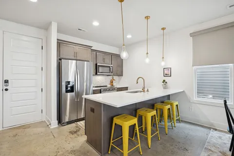 a kitchen with stainless steel appliances kitchen island granite countertop a refrigerator a sink a stove and white cabinets with wooden floor