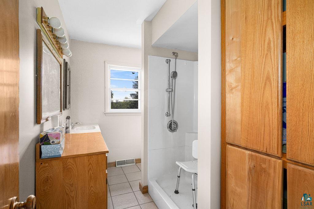 2592 Strandberg Road Barnum, MN 55707 - Photo 17 of 44 Bathroom featuring a vanity with a white sink, wood-finish cabinetry, tile flooring, a window, and a shower stall with a handheld showerhead