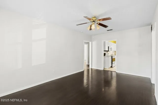 an empty room with wooden floor ceiling fan and windows