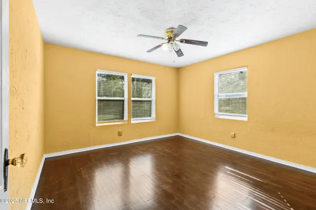 a view of an empty room with wooden floor and a ceiling fan