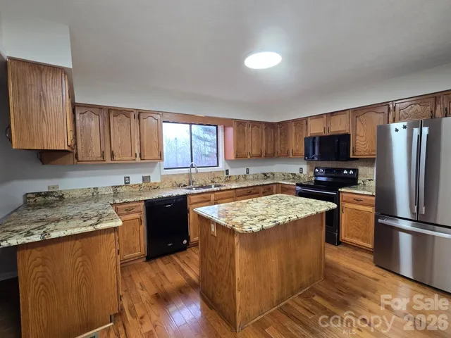 a kitchen with stainless steel appliances granite countertop a stove top oven a refrigerator a sink and dishwasher with wooden floor
