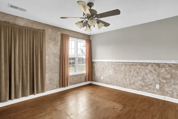 an empty room with wooden floor fan and windows