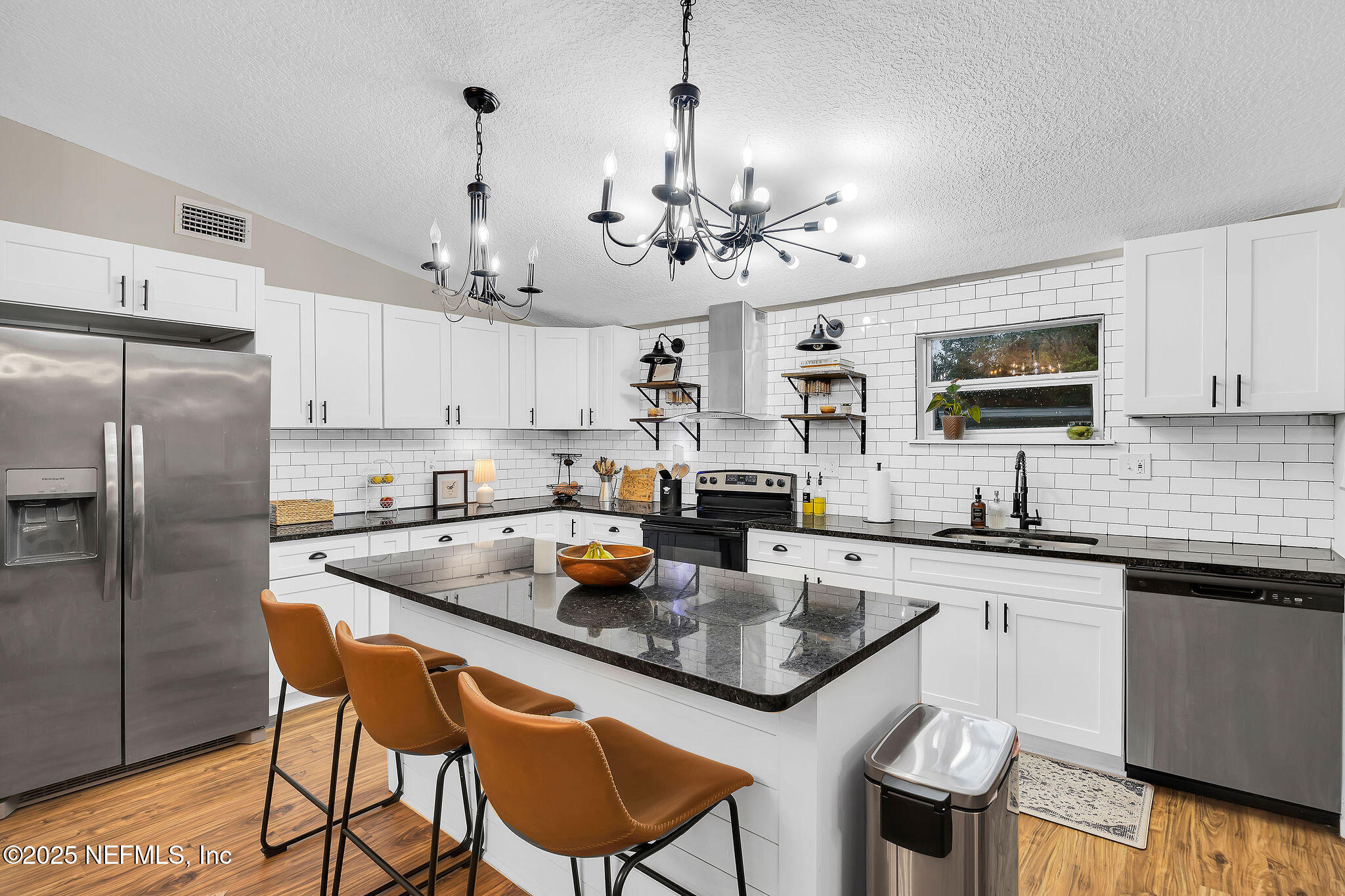 a kitchen with stainless steel appliances granite countertop a sink a stove a refrigerator cabinets and chairs