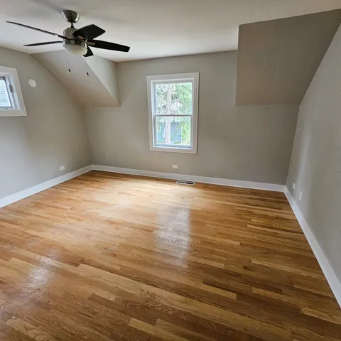 an empty room with wooden floor ceiling fan and windows