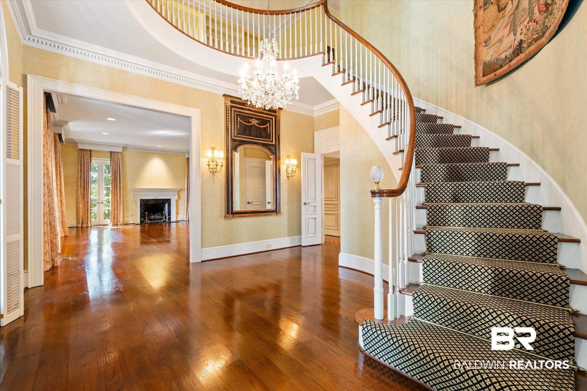 54 Turnin Lane Mobile, AL 36608 - Photo 2 of 35 Staircase with hardwood / wood-style floors, a fireplace, crown molding, a towering ceiling, and a chandelier