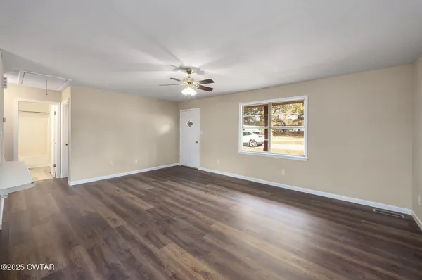 an empty room with wooden floor chandelier fan and windows