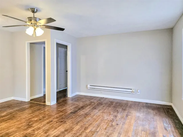 an empty room with wooden floor chandelier fan and windows
