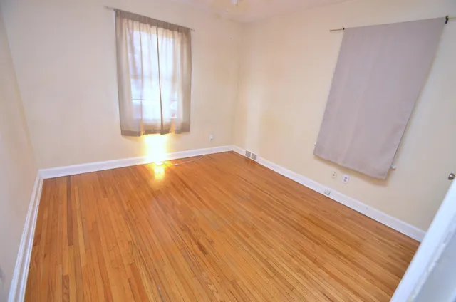 an empty room with wooden floor and windows with curtains