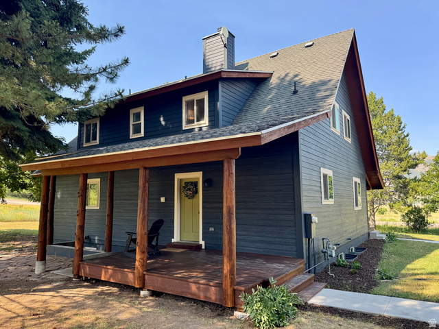 2807 North Ogden Canyon Road Eden, UT 84310 - Photo 69 of 72 Residential exterior featuring dark blue siding, a covered porch with natural wood posts and decking, a light green entry door, a prominent chimney, and multiple windows with white trim