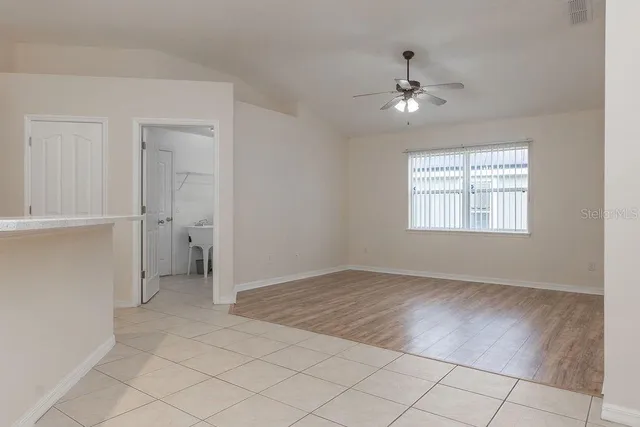 an empty room with chandelier fan and windows