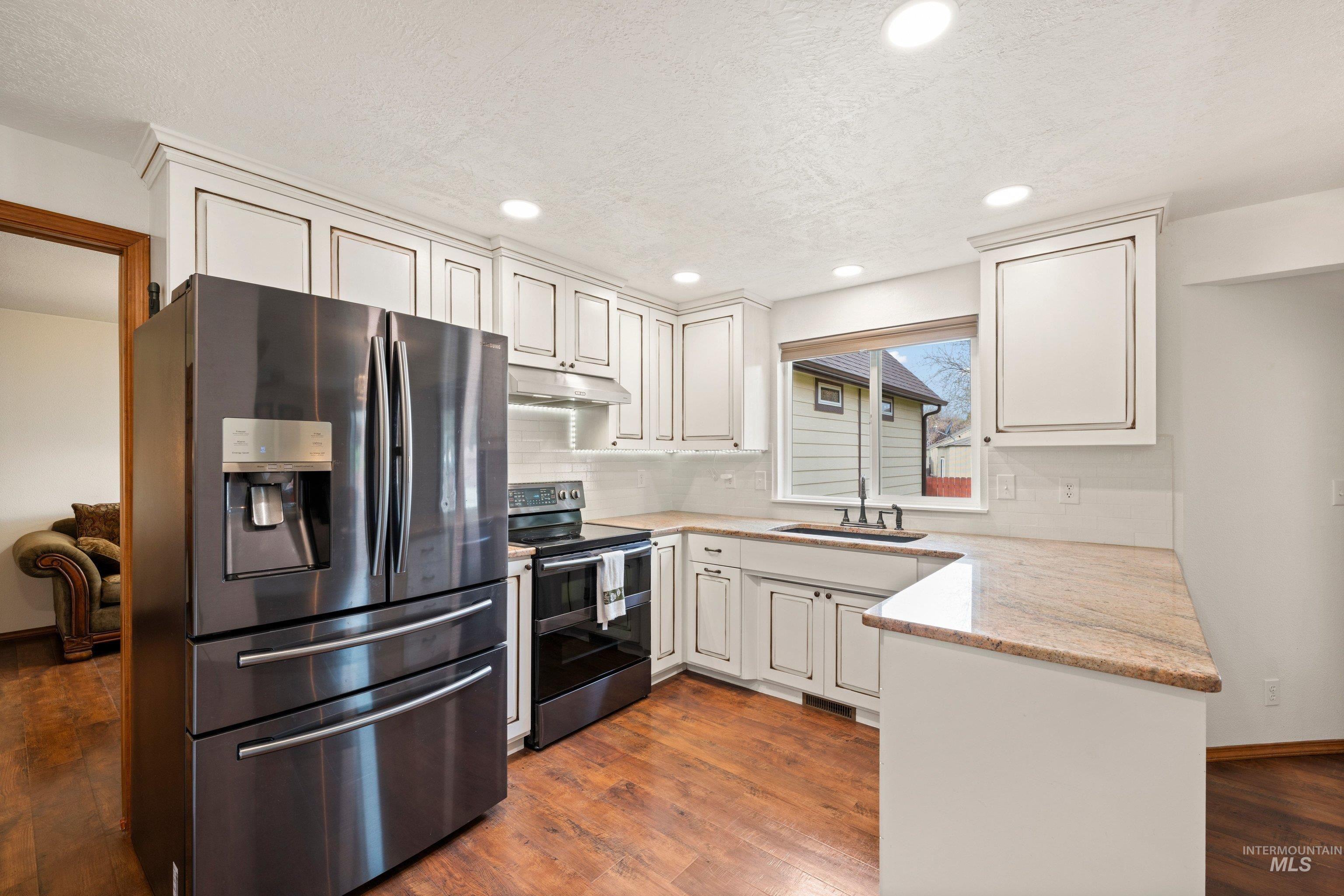 1921 Incline Way Meridian, ID 83646 - Photo 13 of 50 Kitchen featuring white shaker-style cabinetry, wood-finish flooring, a stainless steel range hood, a kitchen sink with a matte black faucet, and light-toned countertops