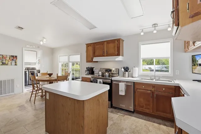 a kitchen with stainless steel appliances kitchen island granite countertop a refrigerator a stove a sink a dining table and chairs with wooden floor