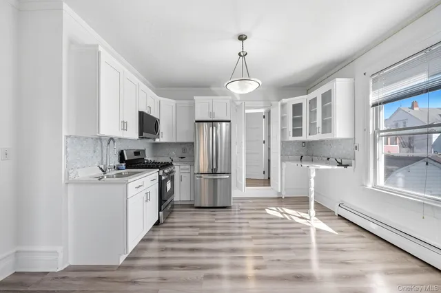 a kitchen with stainless steel appliances granite countertop a refrigerator a stove a sink and white cabinets with wooden floor