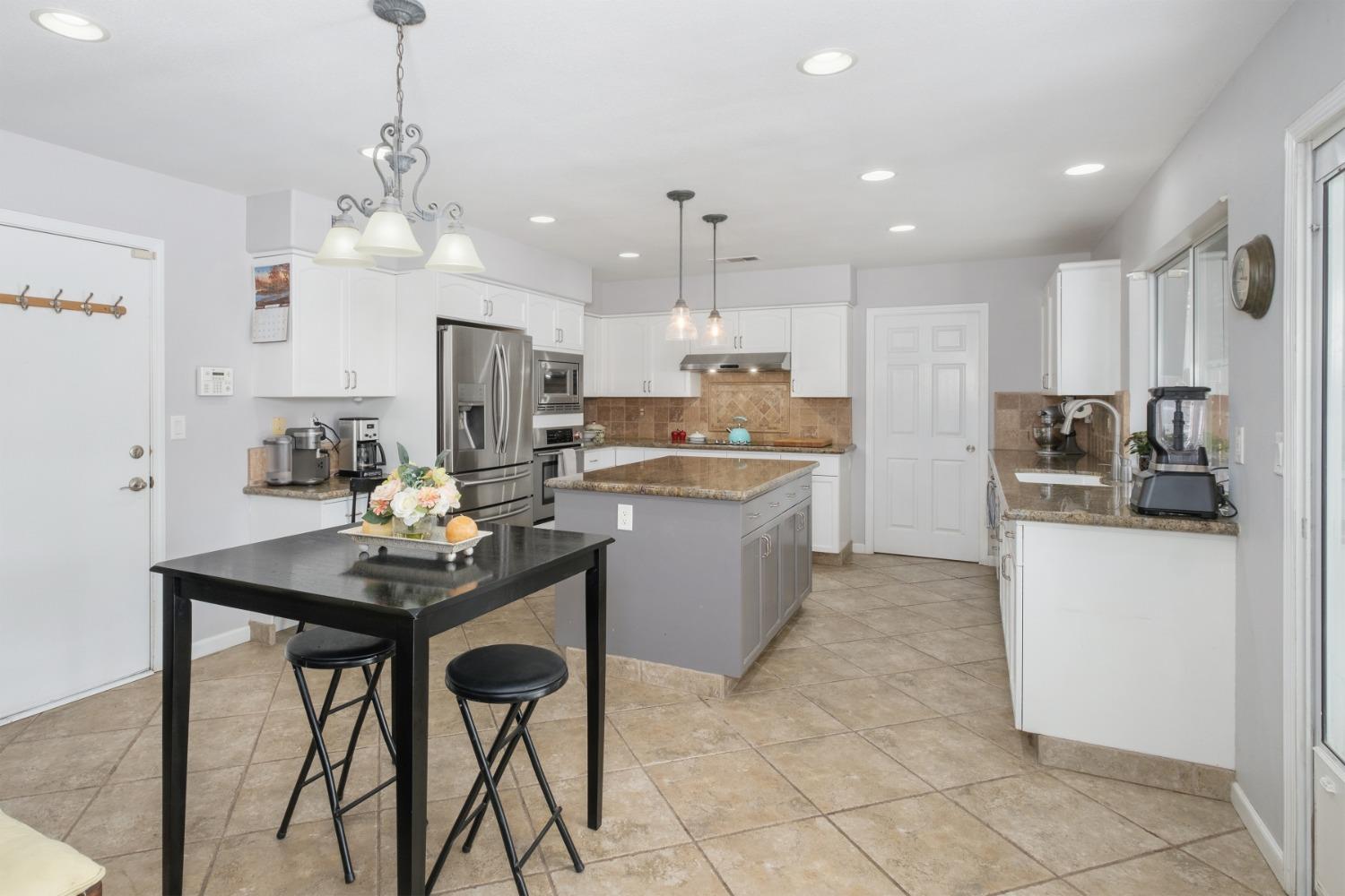 452 Omaha Avenue Clovis, CA 93619 - Photo 9 of 33 a kitchen with stainless steel appliances kitchen island granite countertop a sink a stove a refrigerator cabinets and a dining table with chairs