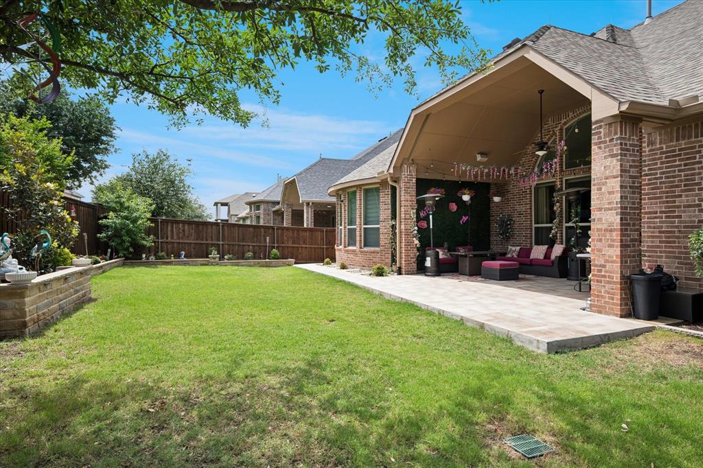 8268 Kara Creek Road Frisco, TX 75036 - Photo 25 of 31 Spacious backyard featuring a covered patio with a ceiling fan, brick exterior, bay window, privacy fencing, and stone retaining wall
