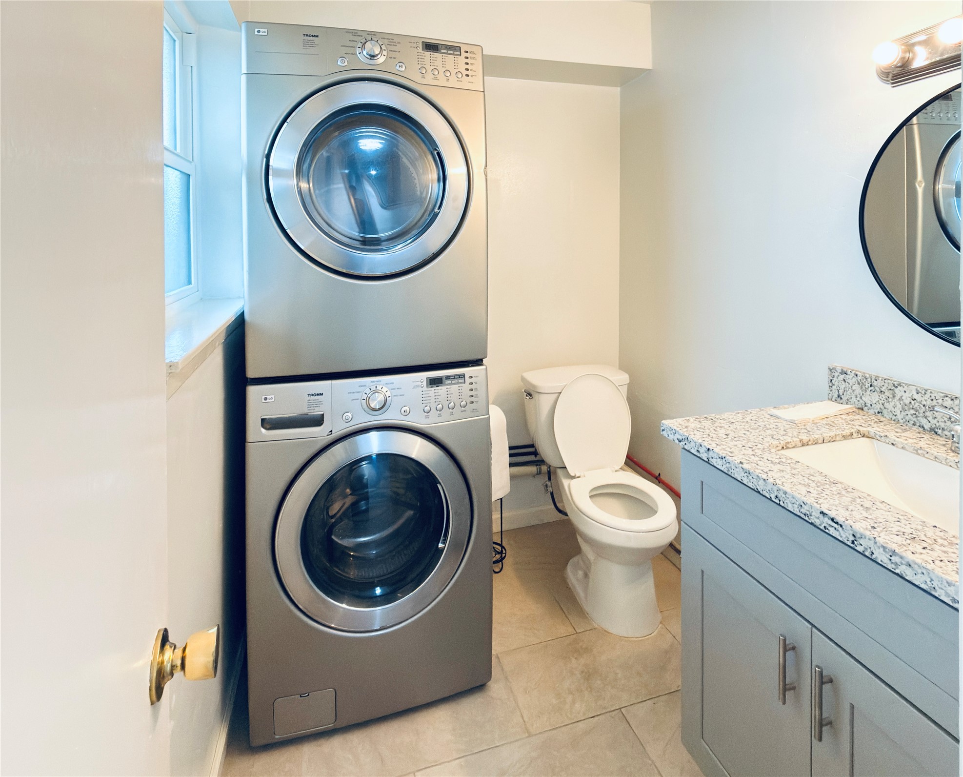 6201 Ranchester Drive, Unit 29 Houston, TX 77036 - Photo 2 of 23 Compact bathroom with modern conveniences, featuring a sleek stackable washer and dryer next to a granite-topped vanity and a toilet.
