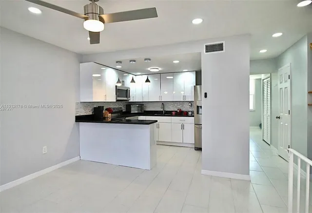 a large white kitchen with a refrigerator a stove and a ceiling fan