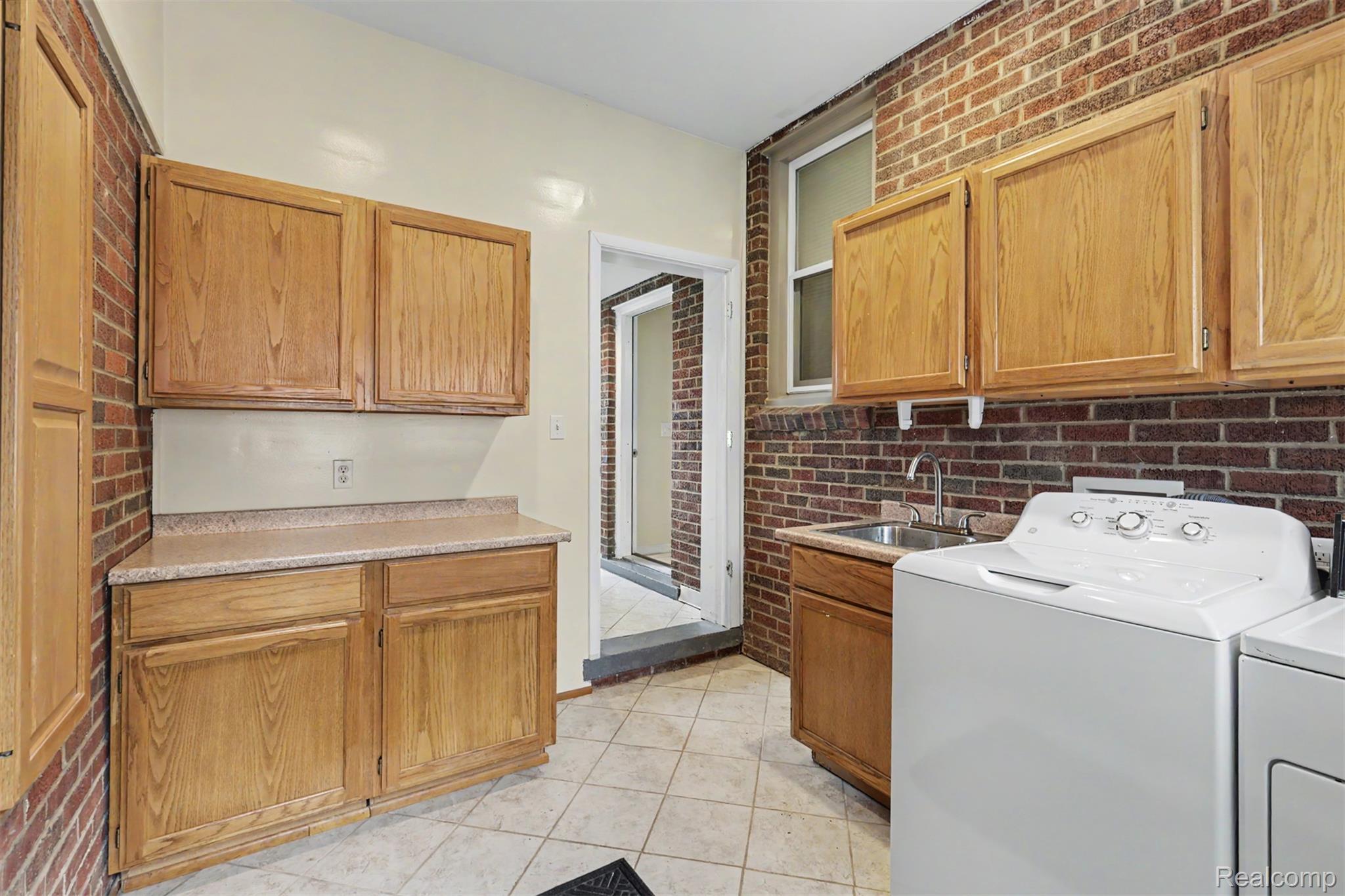 7136 Rosedale Boulevard Allen Park, MI 48101 - Photo 40 of 51 Utility area featuring tile flooring, exposed brick walls, wood cabinetry, and a utility sink
