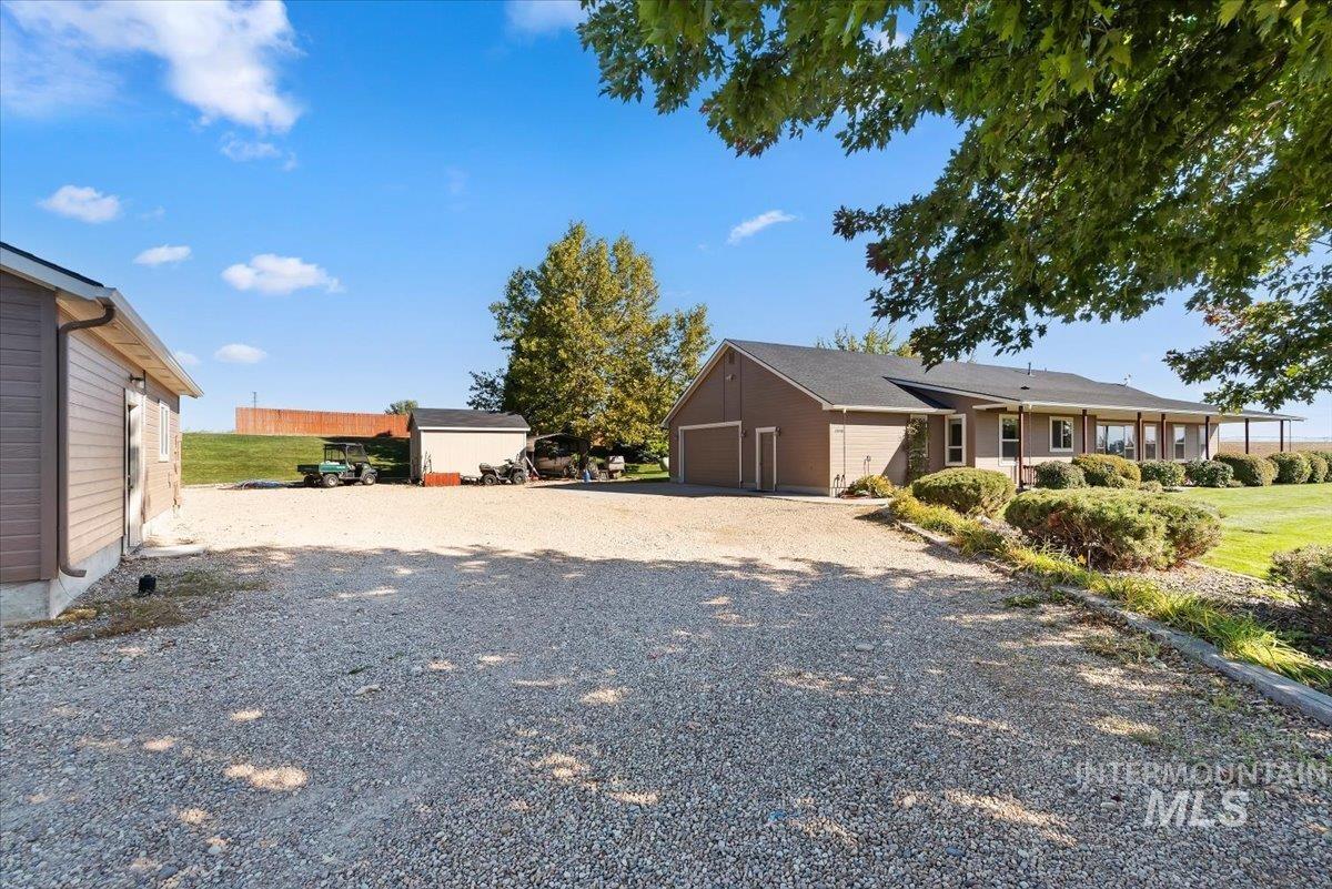 24240 Tiger Lane Caldwell, ID 83607 - Photo 34 of 50 Spacious gravel driveway, attached two-car garage, expansive covered porch, mature trees, and a separate outbuilding