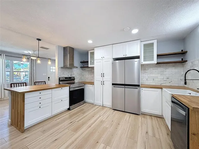 a kitchen with stainless steel appliances granite countertop a refrigerator a sink dishwasher a stove and white countertops with wooden floor