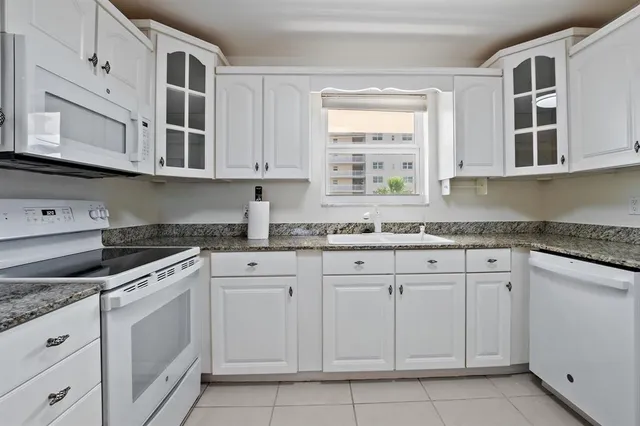 a kitchen with granite countertop white cabinets stainless steel appliances a sink and a window