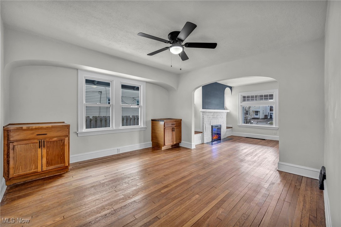 3577 Warren Road Cleveland, OH 44111 - Photo 6 of 17 Unfurnished living room featuring arched walkways, a glass covered fireplace, ceiling fan, baseboards, and hardwood / wood-style flooring