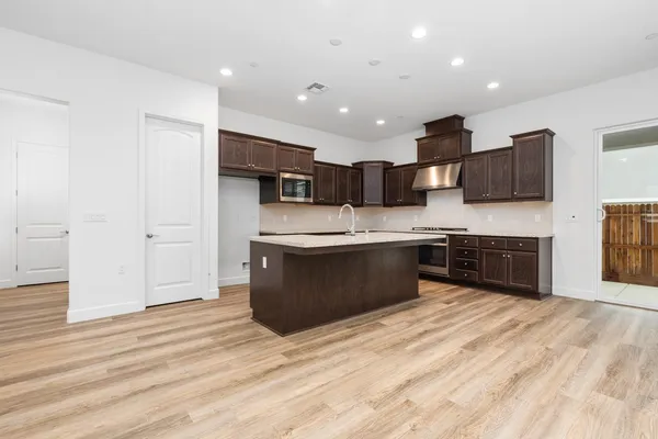 a large kitchen with stainless steel appliances kitchen island a sink dishwasher a stove and a refrigerator with wooden floor