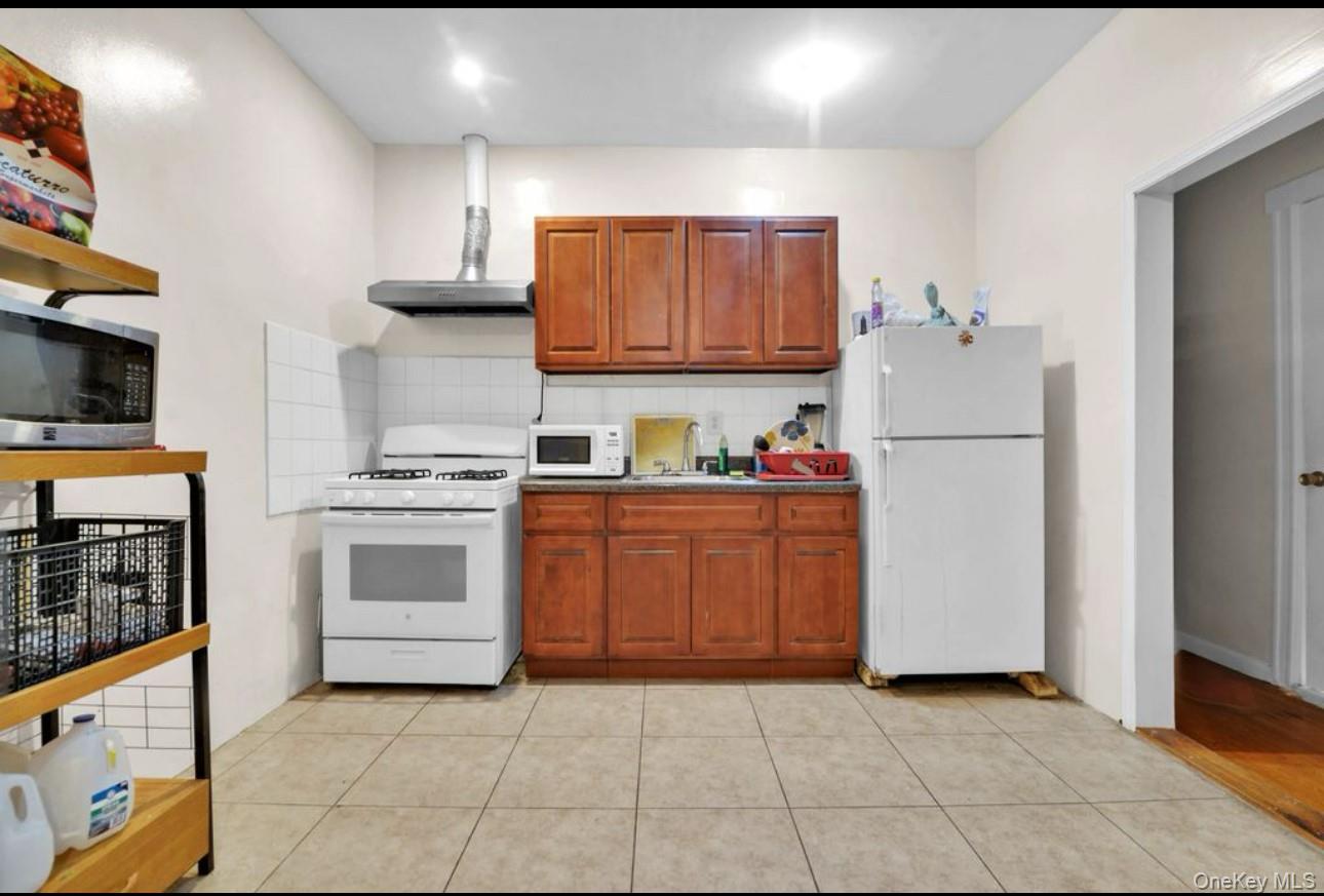 88-22 85th Street Queens, NY 11421 - Photo 14 of 33 Kitchen with decorative backsplash, white appliances, light tile patterned floors, and wall chimney range hood