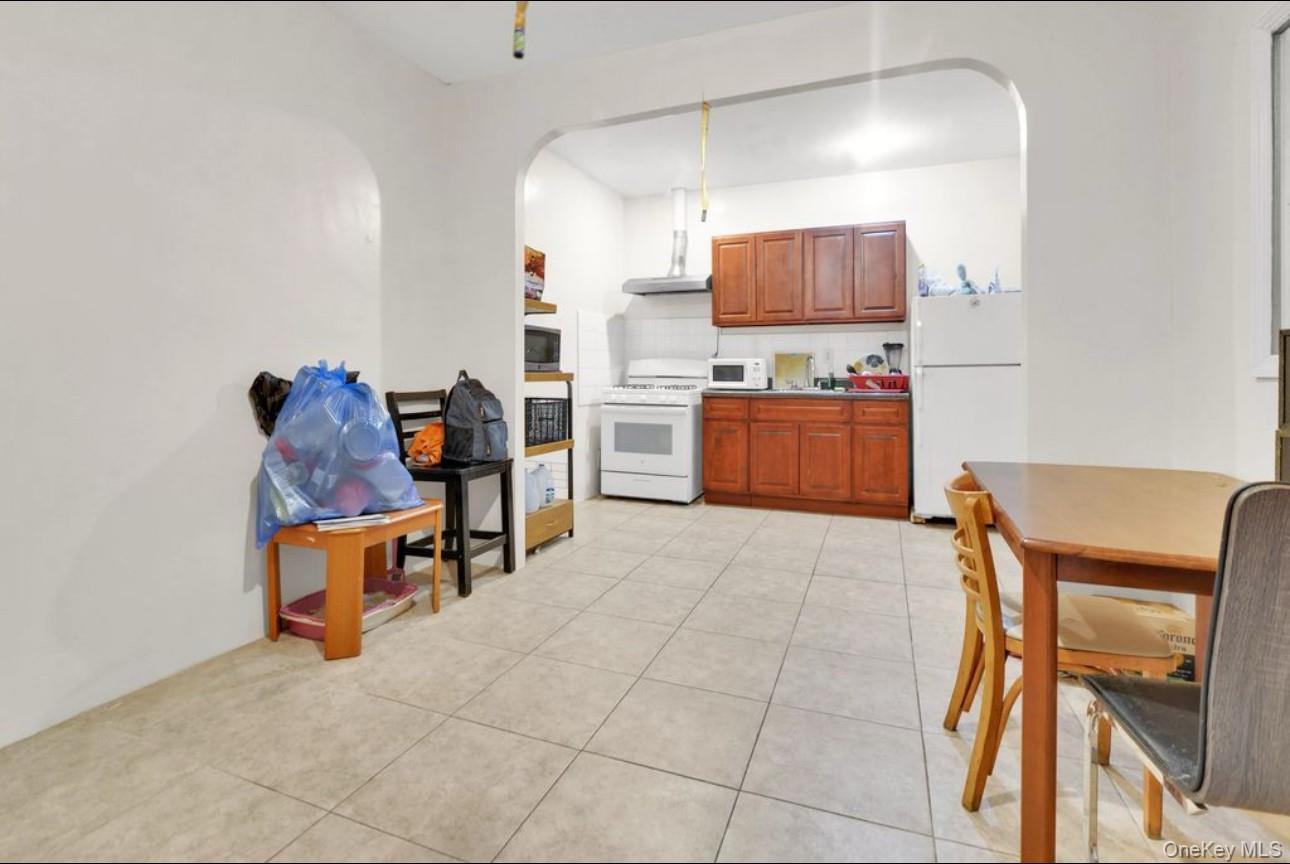 88-22 85th Street Queens, NY 11421 - Photo 16 of 33 Kitchen featuring white appliances, brown cabinets, light tile patterned floors, light countertops, and arched walkways