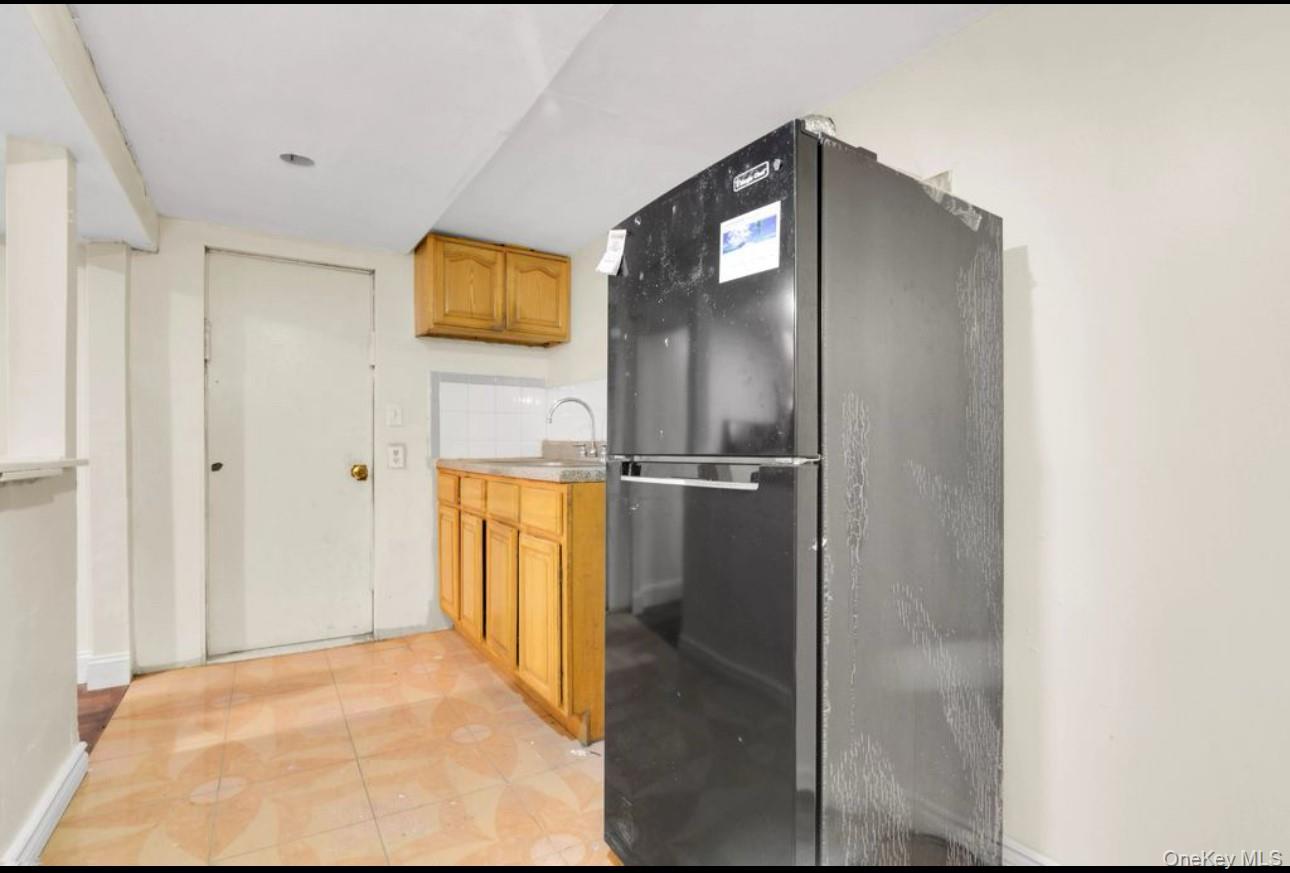 88-22 85th Street Queens, NY 11421 - Photo 30 of 33 Kitchen featuring freestanding refrigerator, light countertops, brown cabinetry, and light tile patterned floors