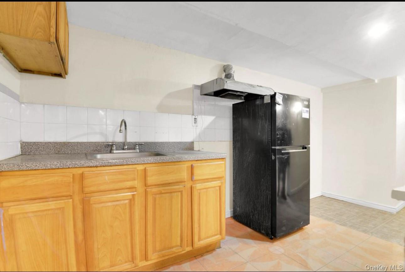 88-22 85th Street Queens, NY 11421 - Photo 31 of 33 Kitchen featuring freestanding refrigerator, decorative backsplash, light countertops, light brown cabinetry, and light tile patterned floors