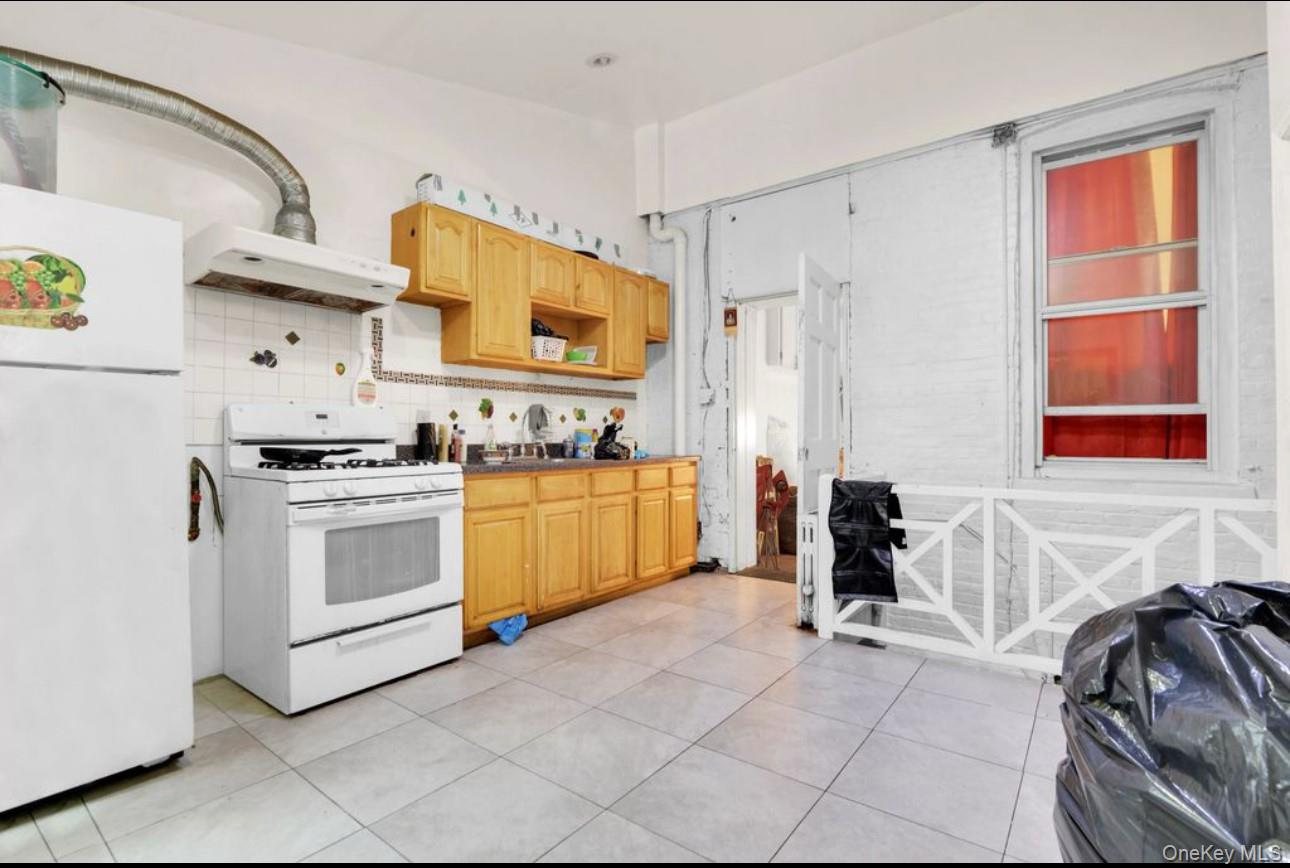 88-22 85th Street Queens, NY 11421 - Photo 10 of 33 Kitchen with white appliances, wall chimney exhaust hood, backsplash, and light tile patterned floors