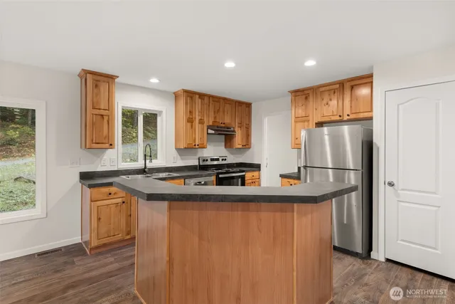 a kitchen with stainless steel appliances granite countertop a refrigerator a stove and a sink with wooden floor