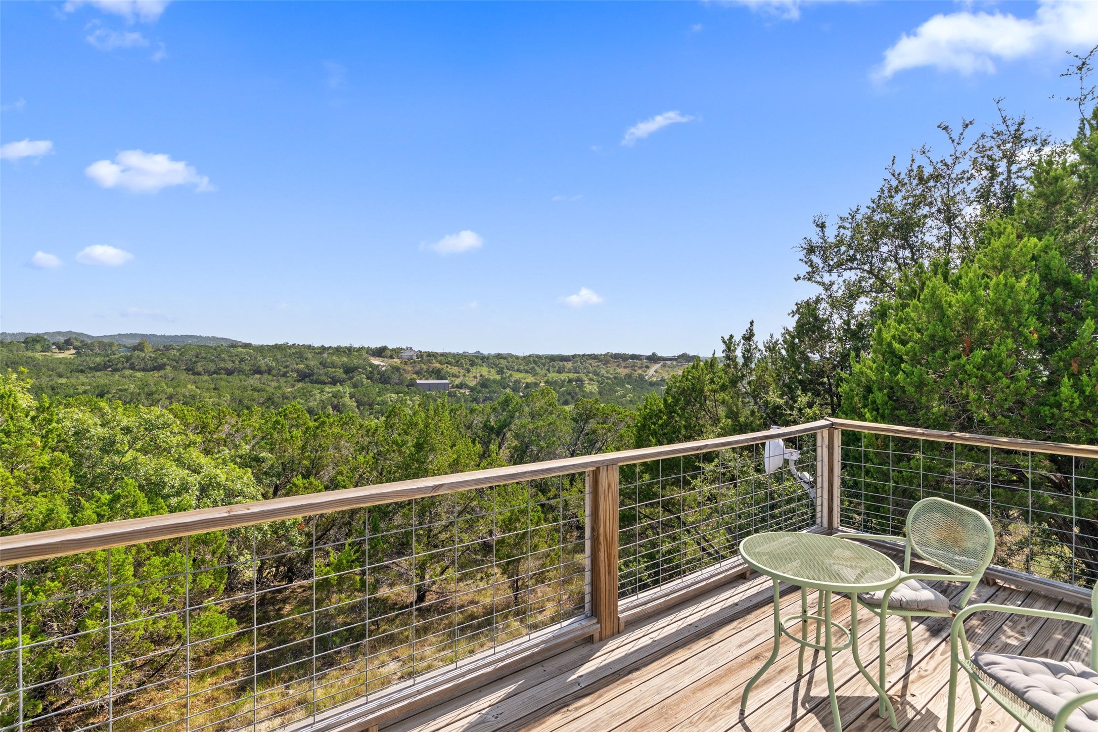 810 Kothmann Road Dripping Springs, TX 78620 - Photo 38 of 40 An elevated wood deck overlooks rolling green hills under a bright blue sky.