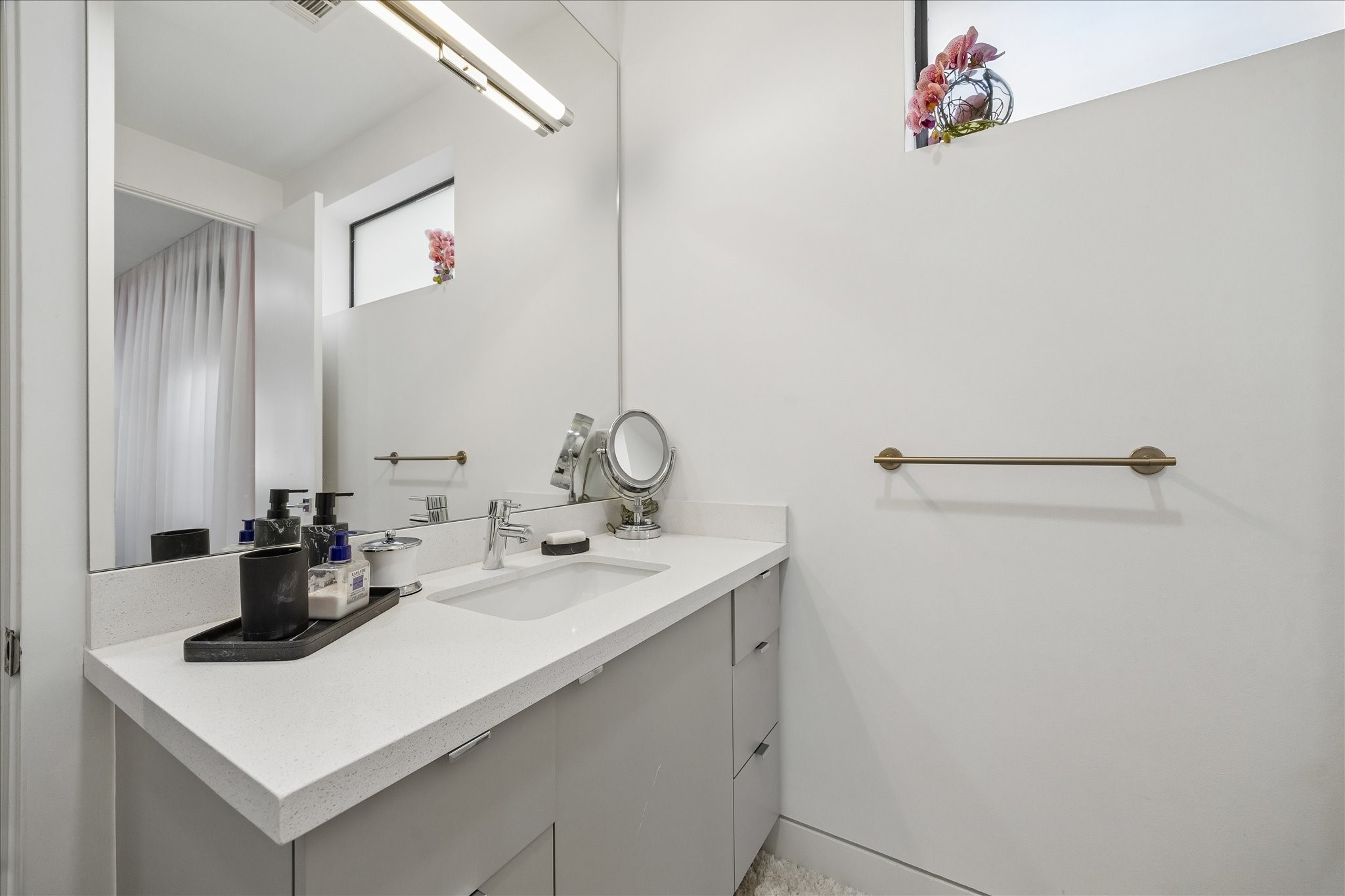 2014 Park Street Houston, TX 77019 - Photo 27 of 40 This modern vanity area features sleek white counter tops with ample storage, a large mirror, and contemporary fixtures. Natural light streams in through a small window, adding brightness to the space.