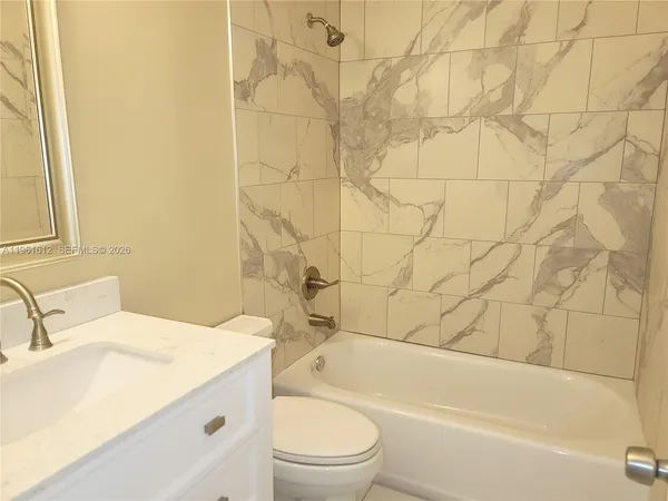 a bathroom with a granite countertop bathtub sink vanity mirror and toilet