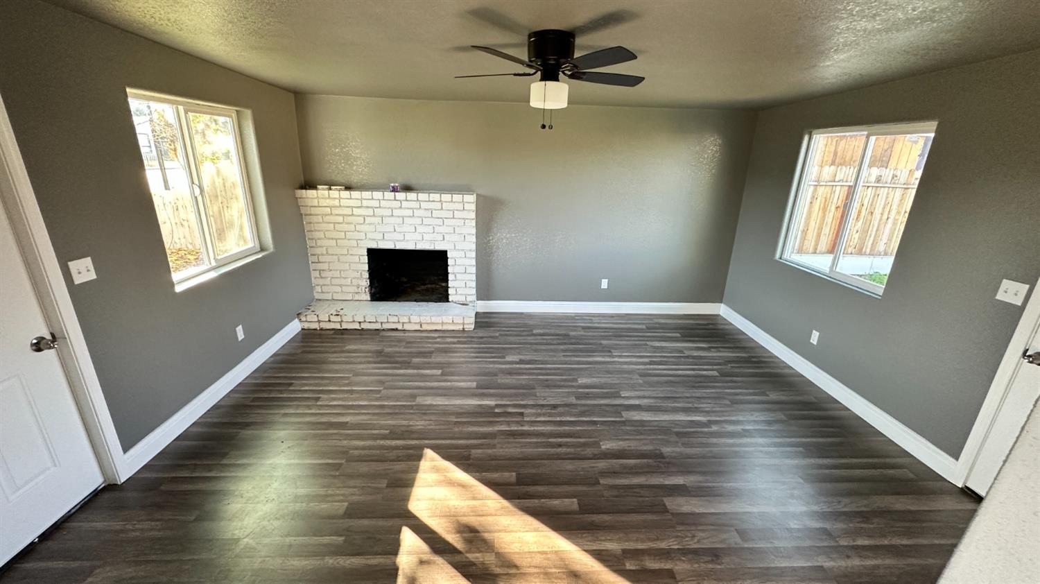 749 East Pleasant Street Coalinga, CA 93210 - Photo 10 of 16 a view of a livingroom with wooden floor a fireplace a ceiling fan and windows