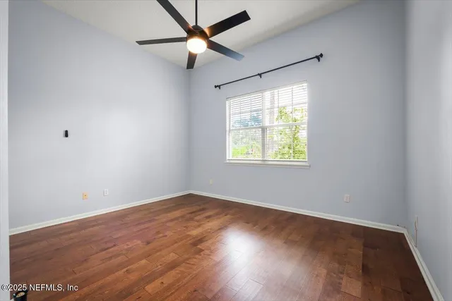 an empty room with wooden floor ceiling fan and windows