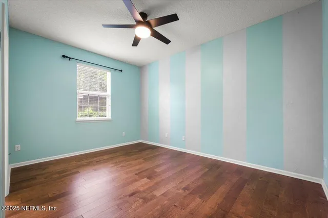 an empty room with wooden floor ceiling fan and windows