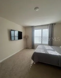 a spacious bedroom with a bed and a flat tv screen on the dresser