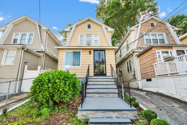 a view of a brick house with large windows and a yard with plants and large tree