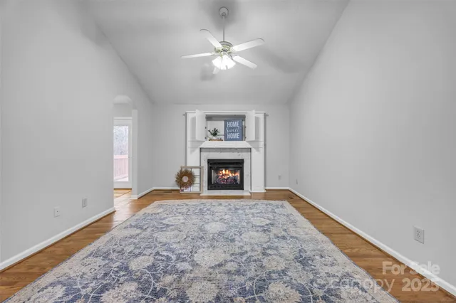 a view of an empty room with chandelier fan and fire place
