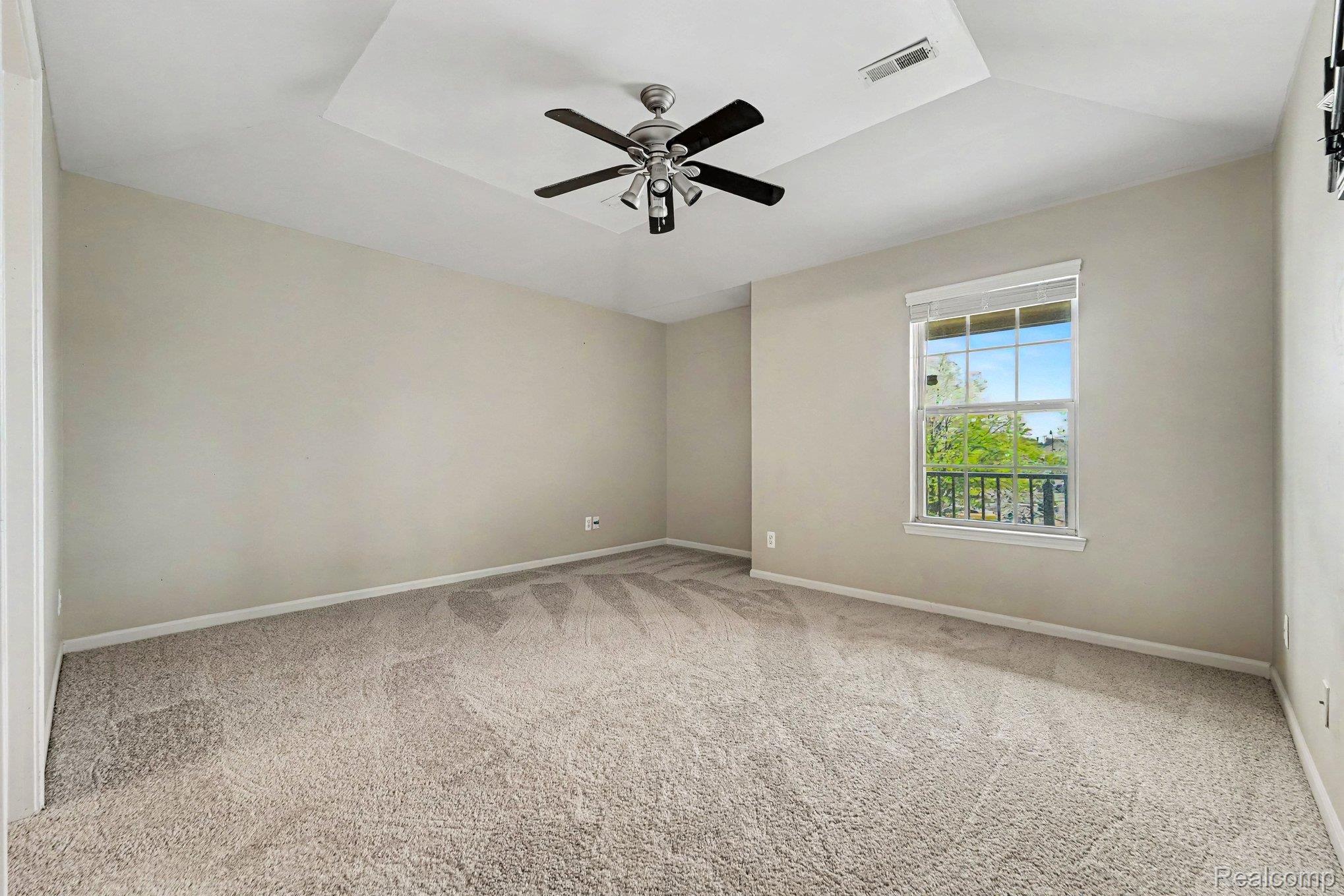 Empty room featuring a tray ceiling, light colored carpet, and ceiling fan