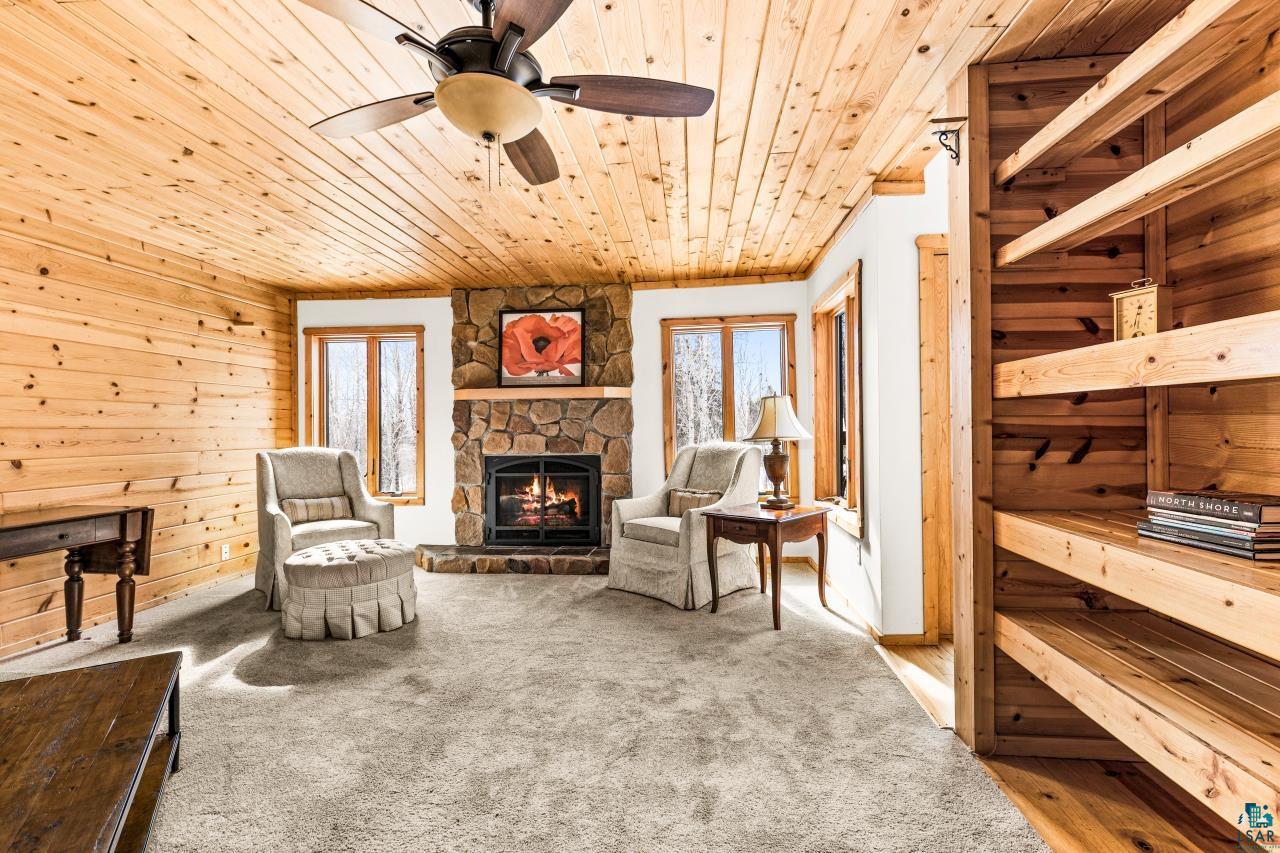67 Snowshoe Trail Tofte, MN 55615 - Photo 13 of 42 Sitting room with plenty of natural light, light carpet, a stone fireplace, wood walls, and wooden ceiling