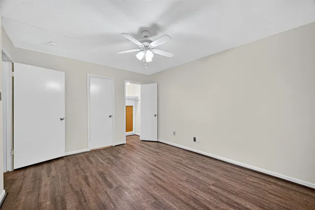 an empty room with wooden floor ceiling fan and windows