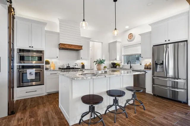 a kitchen with stainless steel appliances granite countertop a sink a stove a refrigerator and island with wooden floor