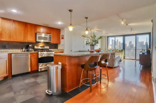 a kitchen with stainless steel appliances granite countertop a refrigerator a stove top oven a sink dishwasher and chairs with wooden floor