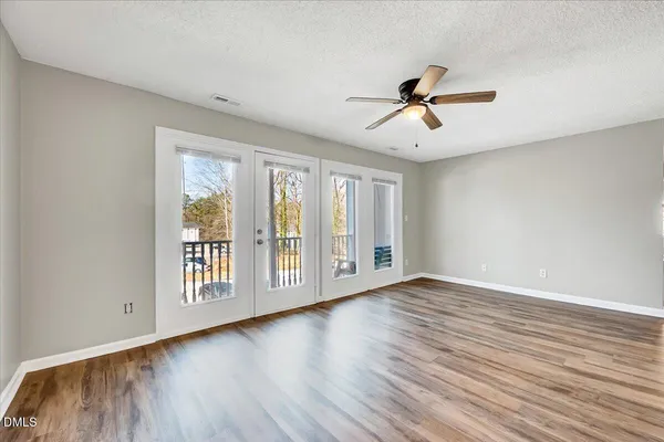 an empty room with wooden floor ceiling fan and windows