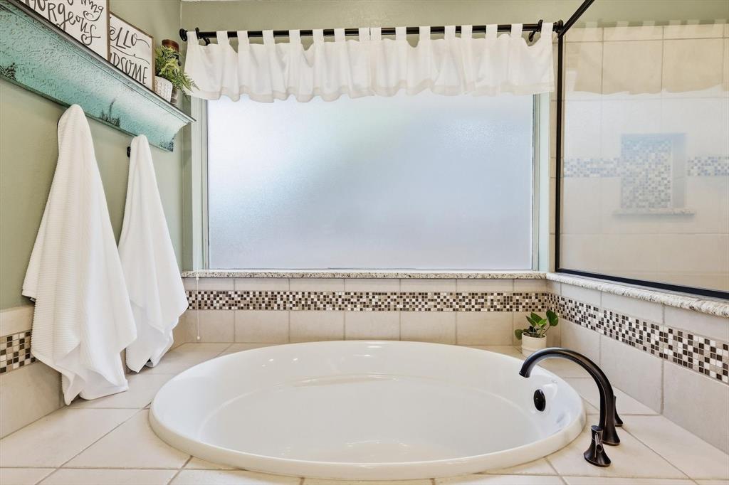 524 Post Oak Road Grapevine, TX 76051 - Photo 28 of 37 Soaking tub with black-finish fixtures, surrounded by tile and mosaic accents, under a large frosted window